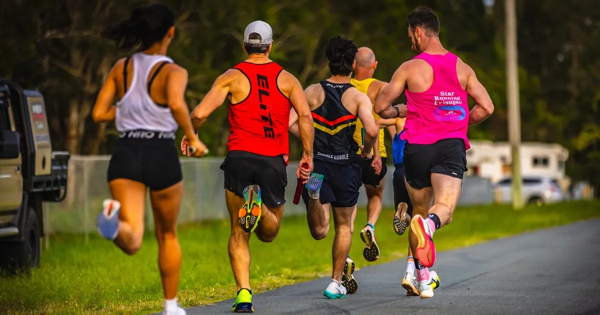 Club runners pass the baton during a relay changeover on the Deagon Speedway track